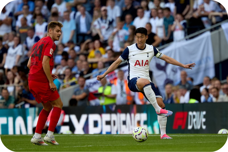 Tottenham-Spieler Heung-Min Son beim Dribbling gegen Münchens Josip Stanišić während eines Spiels vor jubelndem Publikum.